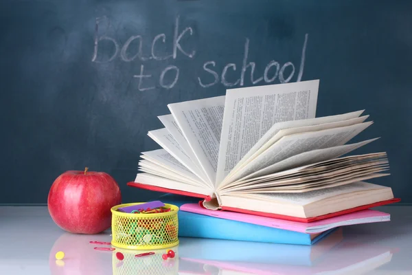 Samenstelling van boeken, briefpapier en een appel op de leraar Bureau in de achtergrond van het bord. terug naar school. — Stockfoto
