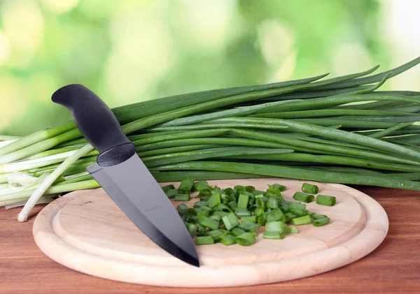 stock image Green onion on a cutting board with knife on green background