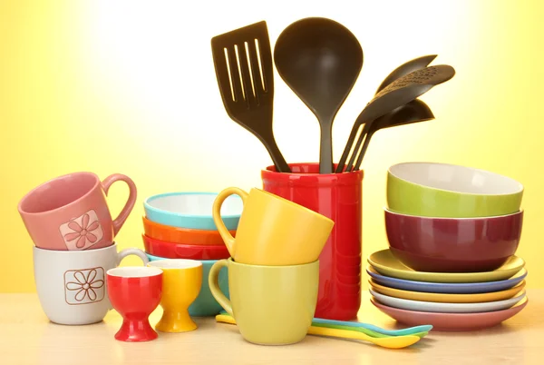 Tigelas vazias brilhantes, copos e utensílios de cozinha em mesa de madeira sobre fundo amarelo — Fotografia de Stock