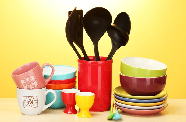 明亮的空碗、 杯子和厨房用具在黄色背景上的木桌上 — 图库照片