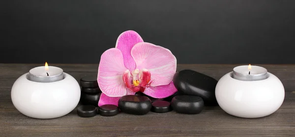 Курортные камни с цветком орхидеи и свечами на деревянном столе на сером фоне — стоковое фото