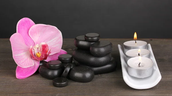 Spa kamienie z orchidea kwiat i świece na drewnianym stole na szarym tle — Zdjęcie stockowe