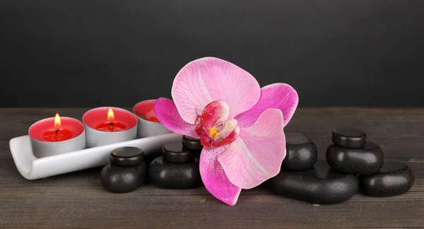 Σπα πέτρες με ορχιδέα λουλούδι και κεριά στο ξύλινο τραπέζι σε γκρι φόντο — Φωτογραφία Αρχείου