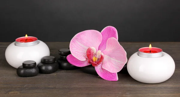Spa-stein med orkideblomst og lys på trebord på grå bakgrunn – stockfoto