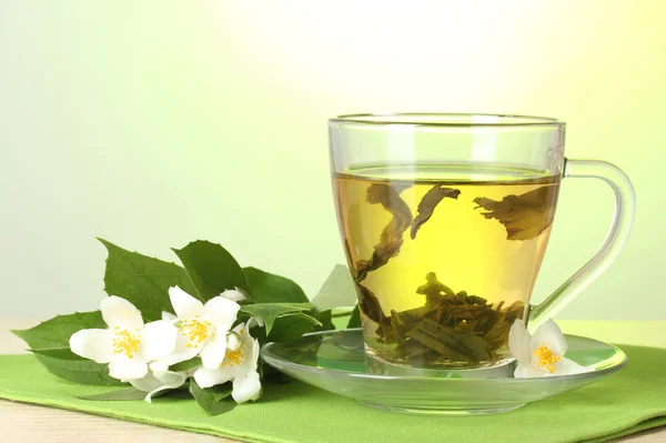 Cup of green tea with jasmine flowers on wooden table on green background — Stock Photo, Image