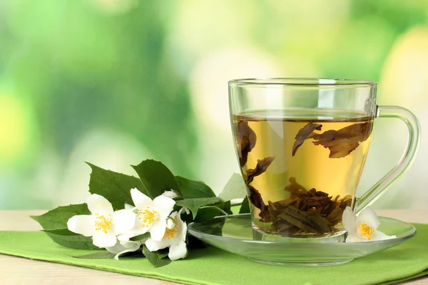 Φλιτζάνι πράσινο τσάι με γιασεμί λουλούδια στο ξύλινο τραπέζι σε πράσινο φόντο — Φωτογραφία Αρχείου