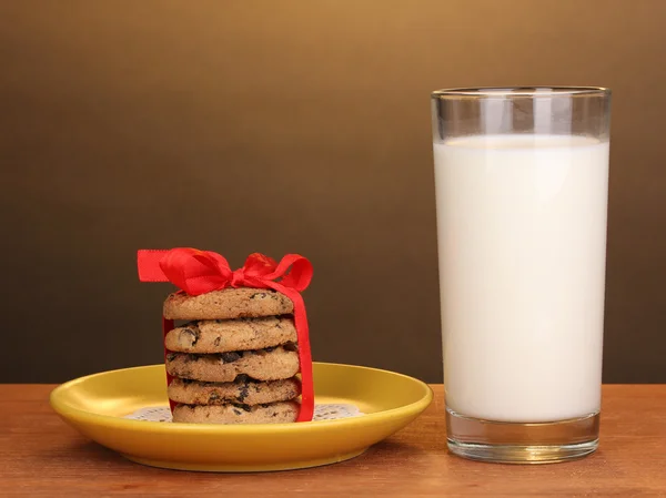 Vaso de leche y galletas sobre mesa de madera sobre fondo marrón —  Fotos de Stock