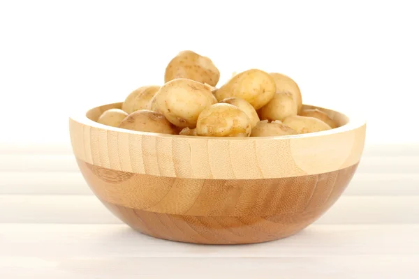 Batatas jovens em uma tigela de madeira em mesa de madeira branca close-up — Fotografia de Stock