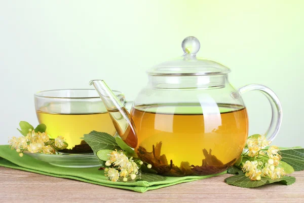 Teekanne und Tasse mit Lindentee und Blumen auf Holztisch auf grünem Hintergrund — Stockfoto