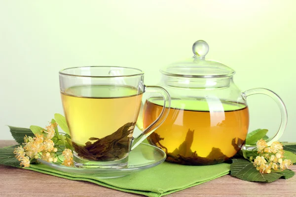 Tekanna och kopp med linden te och blommor på träbord på grön bakgrund — Stockfoto