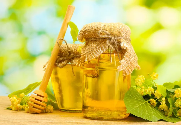 Burkar med linden honung och blommor på träbord på grön bakgrund — Stockfoto