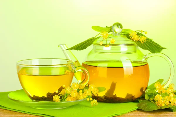 Czajnik i filiżanki herbaty lipy i kwiaty na drewnianym stole na zielonym tle — Zdjęcie stockowe