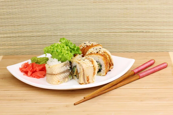 Tasty rolls served on white plate with chopsticks on wooden table on light background — Stock Photo, Image