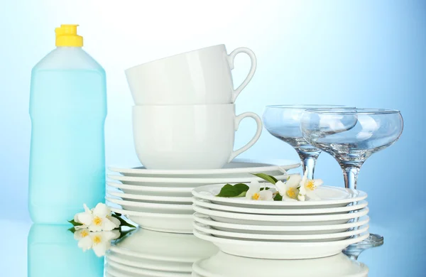 Platos limpios vacíos, tazas y vasos con líquido lavavajillas y esponjas sobre fondo azul — Foto de Stock