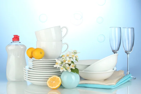 Leere Teller, Gläser und Tassen mit Spülmittel und Zitrone auf blauem Hintergrund — Stockfoto