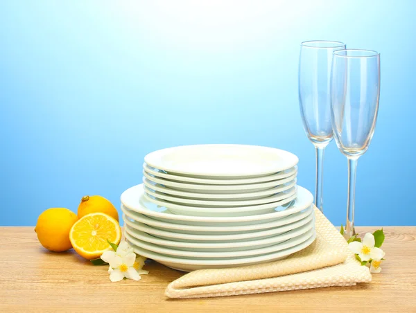 Pratos limpos vazios e copos e limão na mesa de madeira no fundo azul — Fotografia de Stock