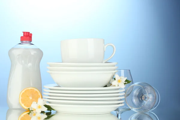 Prázdné čisté talíře, sklenice a kelímky s saponátů a citron na modrém pozadí — Stock fotografie