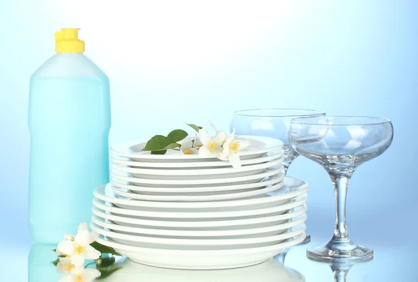 Platos y vasos limpios vacíos con líquido lavavajillas sobre fondo azul — Foto de Stock