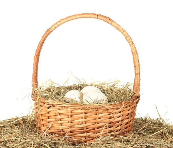 Huevos blancos en una canasta de mimbre sobre heno sobre fondo blanco de cerca — Foto de Stock