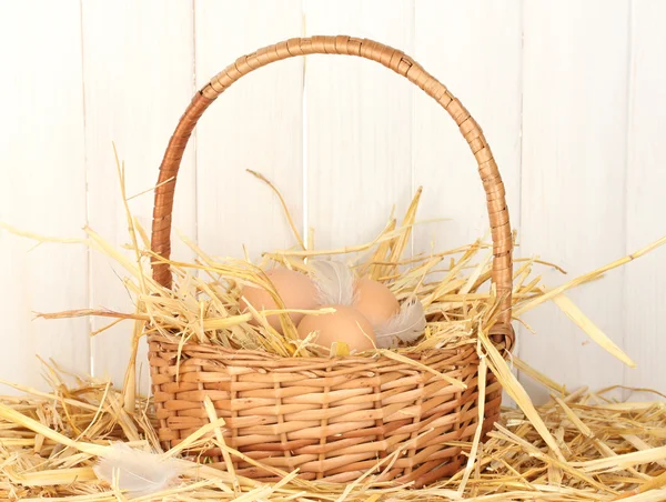 Barna tojás a fonott bascet a szalmát, fehér fa háttér — Stock Fotó