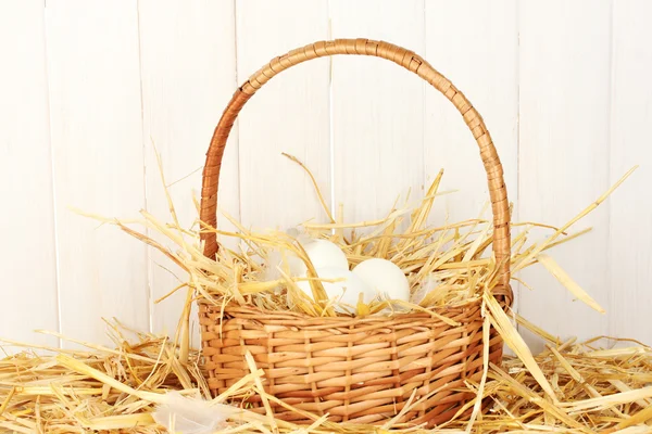 White eggs in a wicker bascet on straw on white wooden background — Stock Photo, Image
