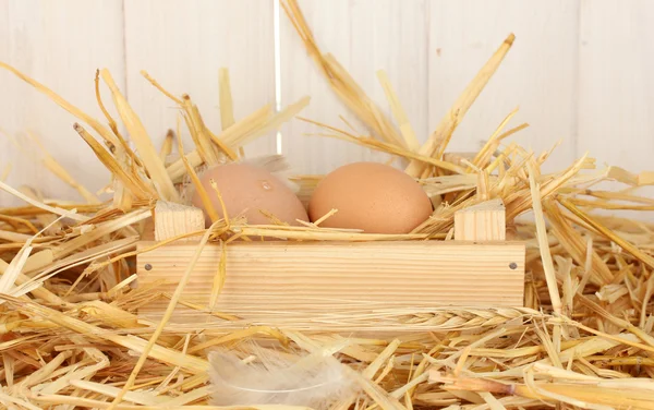 Braune Eier in einer Holzkiste auf Stroh auf weißem Holzgrund — Stockfoto