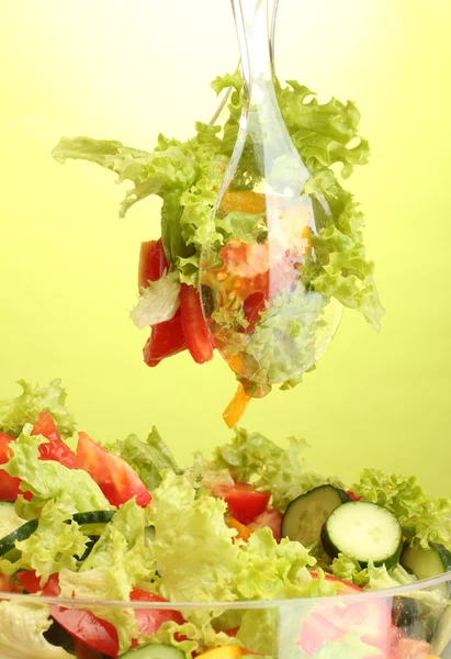 Färska grönsaker sallad i transparent skål med sked och gaffel på grön bakgrund — Stockfoto