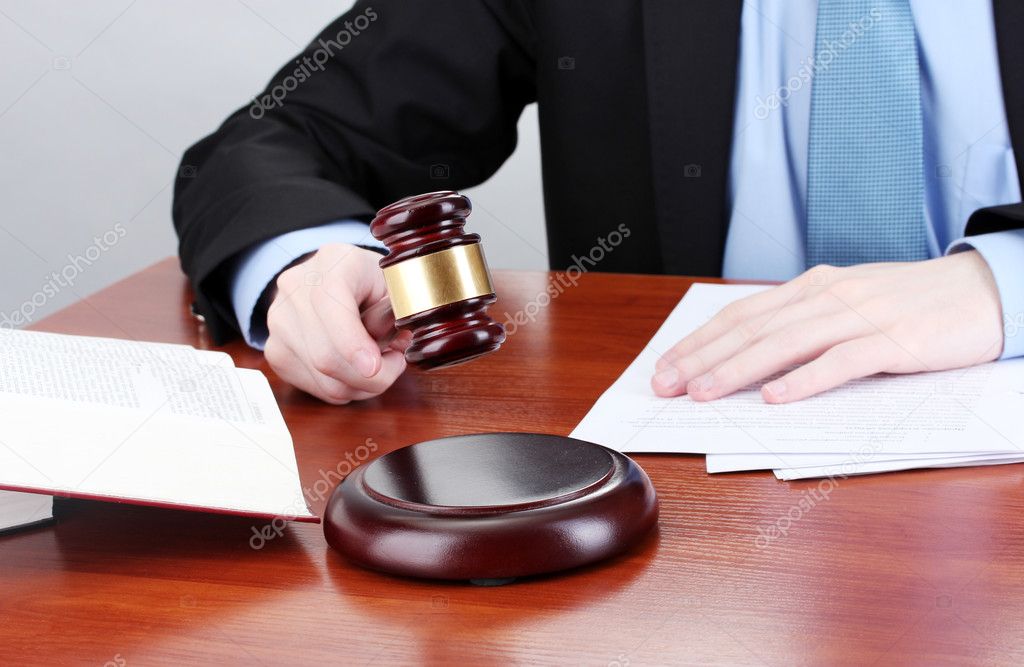 Wooden gavel in hand and books on wooden table on gray background