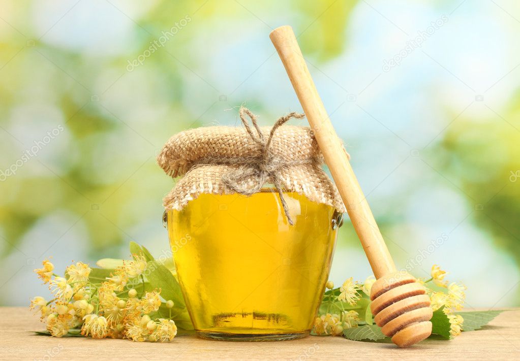 Jar with linden honey and flowers on wooden table on green background