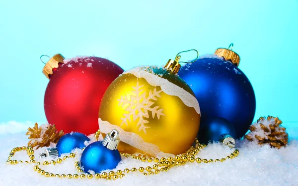 Krásné světlé vánoční koule a šišky ve sněhu na modrém pozadí — Stock fotografie