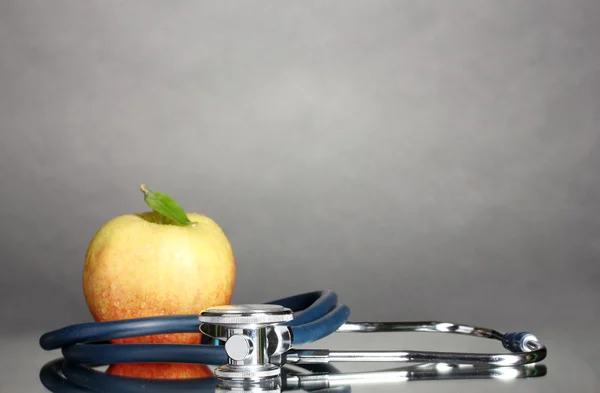 Medical stethoscope and apple on grey — Stock Photo, Image