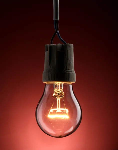 Uma lâmpada acesa no fundo vermelho — Fotografia de Stock