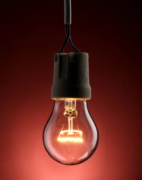 stock image A lit light bulb on red background