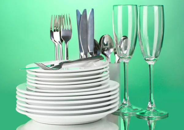 Čisté talíře, sklenice a příbory na zeleném pozadí — Stock fotografie