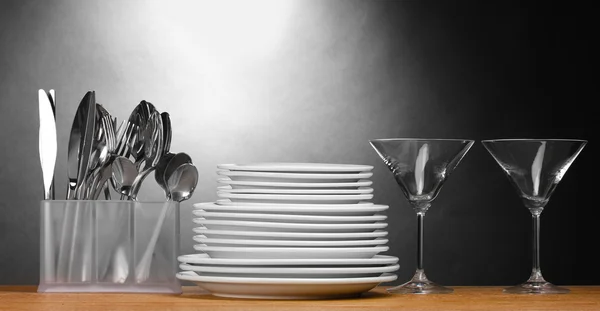 Placas limpias, vasos y cubiertos sobre mesa de madera sobre fondo gris —  Fotos de Stock