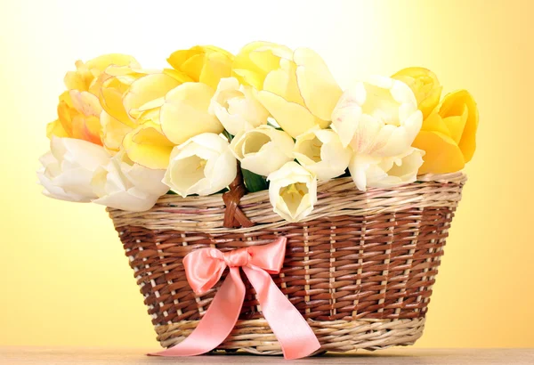 Красивые тюльпаны в корзине на деревянном столе на желтом фоне — стоковое фото