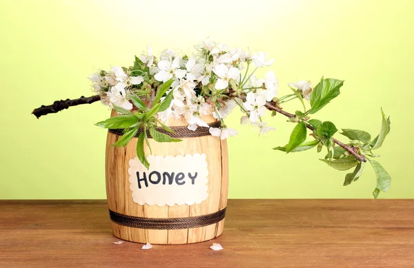 Sweet honey in barrel with blossoming branch on wooden table on green background — Stock Photo, Image