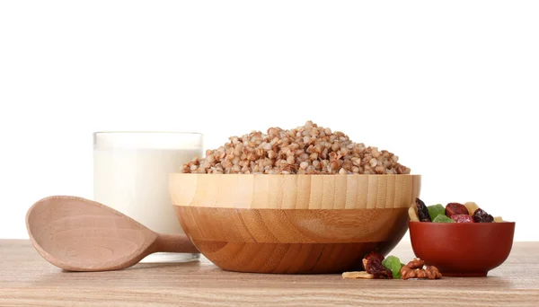 Boiled buckwheat in a wooden bowl with a glass of milk on wooden table isolated on white — Stock Photo, Image