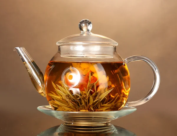 Скляний чайник з екзотичним зеленим чаєм на дерев'яному столі на коричневому фоні — стокове фото