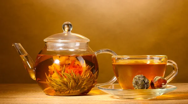 Bule de vidro e xícara com chá verde exótico na mesa de madeira no fundo marrom — Fotografia de Stock