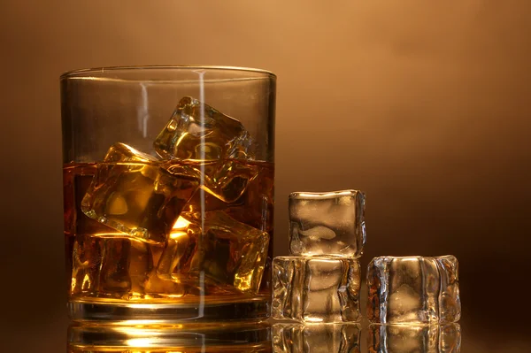 stock image Glass of whiskey and ice on brown background