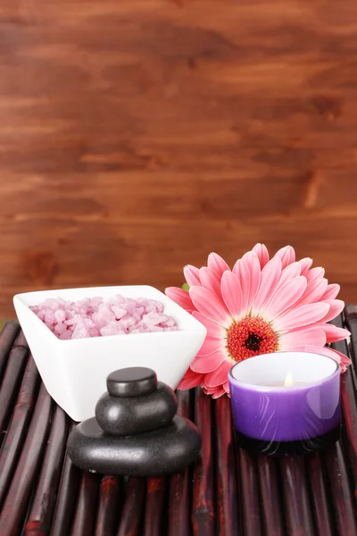 Composition of spa stones, bath salt, candle and gerbera on bamboo mat on wooden background — Stock Photo, Image