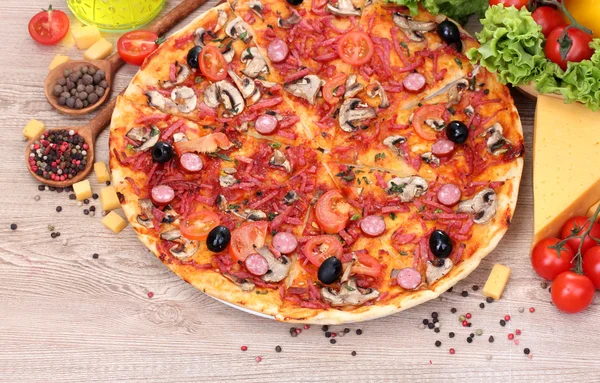 Pyszne pizzy i warzywa na drewnianym stole — Zdjęcie stockowe