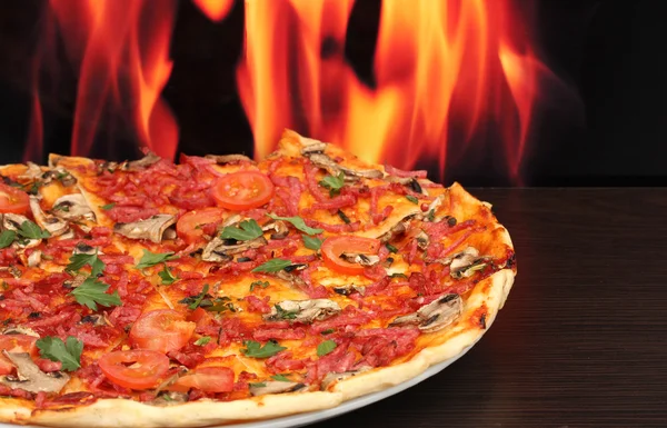 Leckere Pizza mit Gemüse und Salami auf Holztisch auf Flammenhintergrund — Stockfoto