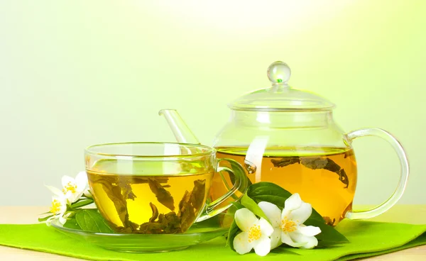 Grönt te med jasmine i kopp och tekanna på träbord på grön bakgrund — Stockfoto
