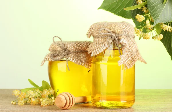 Jars with linden honey and flowers on wooden table on green background