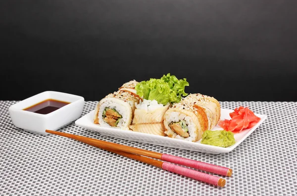 Вкусные рулоны подаются на белой тарелке с палочками для еды на сером фоне — стоковое фото