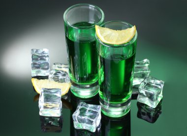 Two glasses of absinthe, lemon and ice on green background clipart