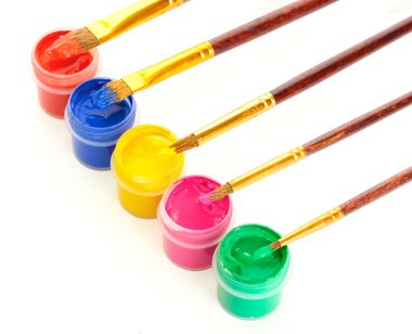 Brushes on the jars with colorful gouache on white background close-up