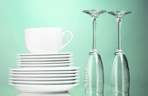 Clean plates, cup and glasses on green background — Stock Photo, Image